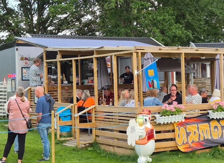 En grupp människor som står och sitter på en uteservering vid en kiosk
