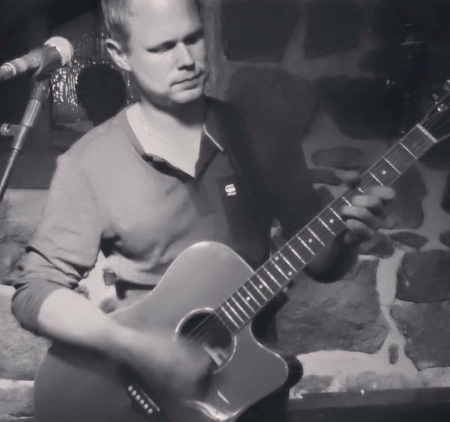 En man spelar gitarr framför en mikrofon.
