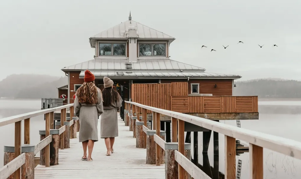 Två personer går längs en brygga mot ett hus.