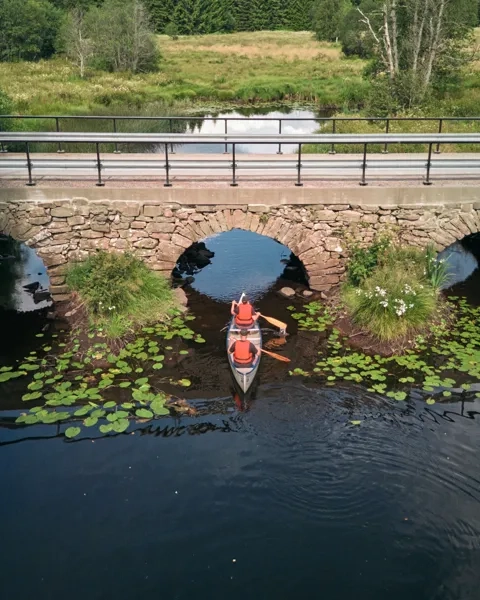 En person i en kanot på en flod under en bro.