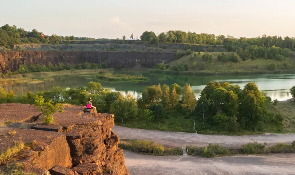 Kvinna sitter och blickar ut över stenbrott och damm i kvällsljus