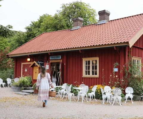 Kvinna går på en grusväg utanför en röd stuga.