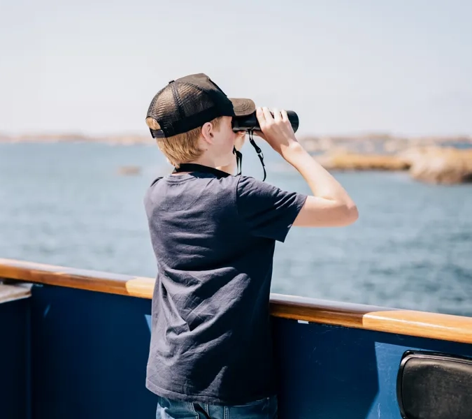 A boy looking through binoculars on a boat.