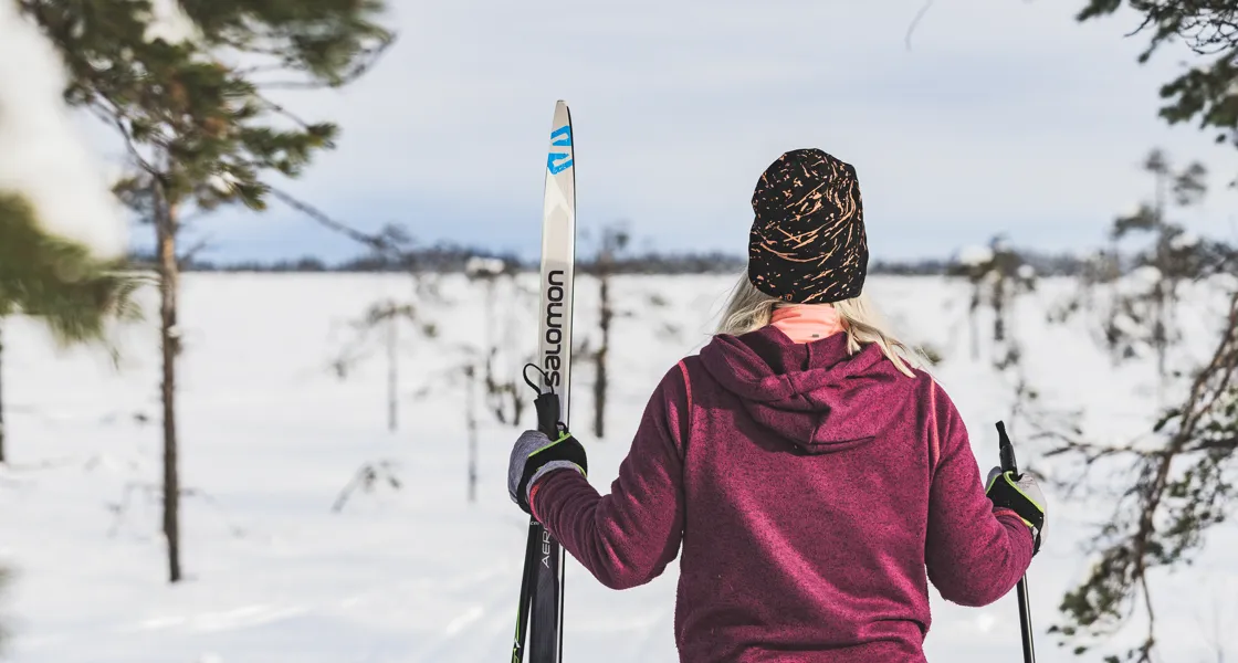 En person som går och bär ett par skidor in i en skog
