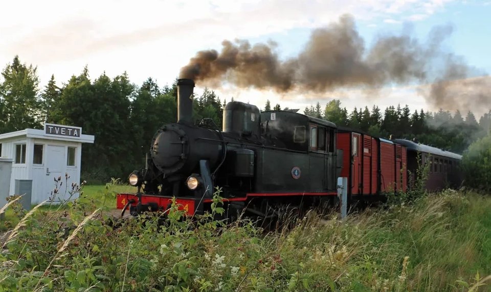 Ett svart ånglok åker förbi en vit kur med  en skylt med texten TVETA.