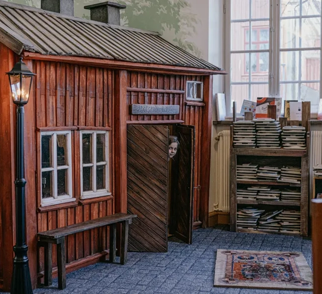 Ett rum fyllt med hus i miniatyr. Ett barn tittar ut genom dörren på miniatyrhuset.