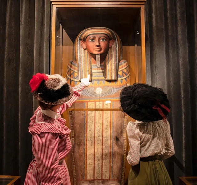 Två kvinnor i hattar tittar på en sarkofag