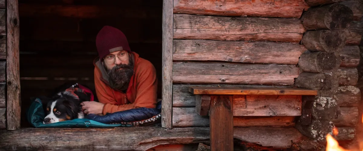 Ein Mann mit Bart, der mit einem Hund in einem Fenster sitzt.