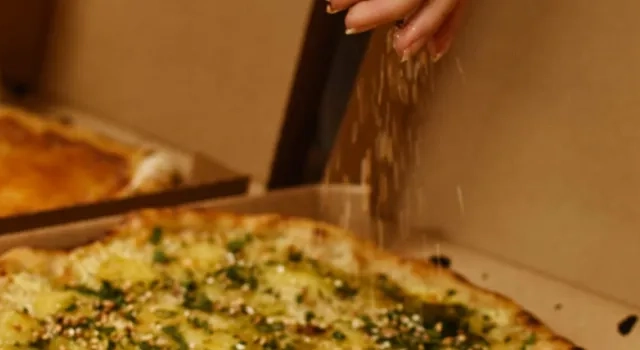 En person som tar en bit pizza ur en låda.