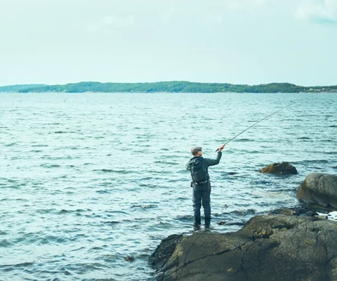 En man som står på en klippa intill ett vattendrag.
