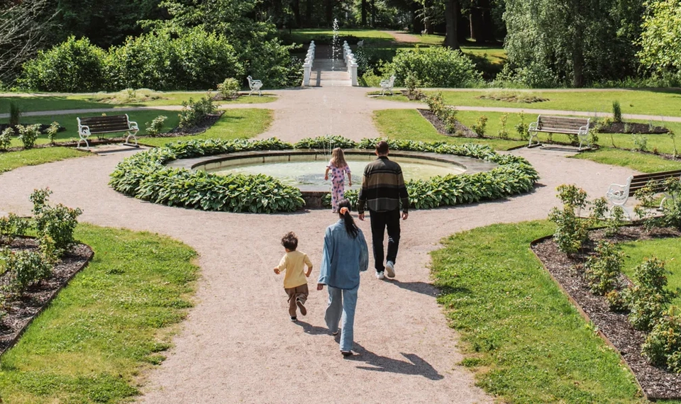 En kvinna och två barn går genom en trädgård.