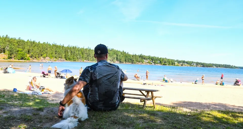 Man med hund sitter vid en sandstrand