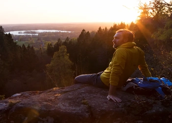 En man sitter på en klippa med utsikt över en sjö.