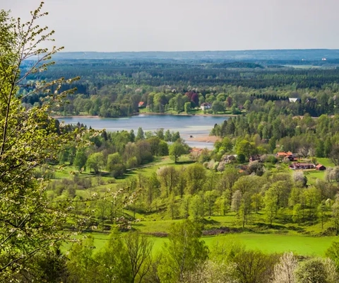 Utsikt över Valle med gröna ängar, körsbärsträd som är på väg att slå ut, sjöar och långt bort i horisonten syns berget Kinnekulle och Vänern.