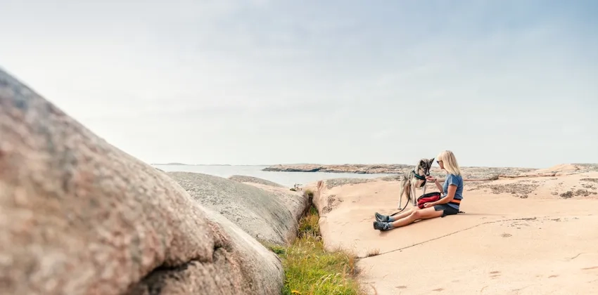 En kvinna sitter på en klippa med en hund intill ett vattendrag.