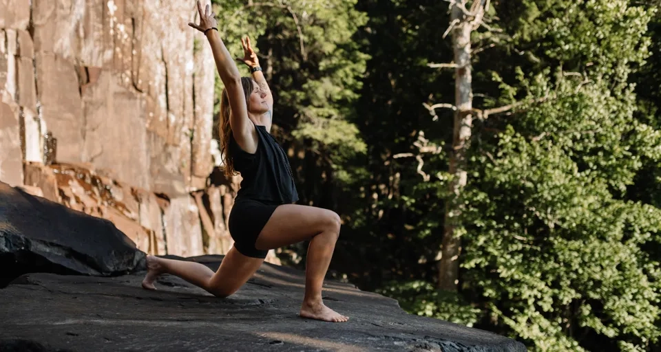 En kvinna yogar på en klippa intill en skog.
