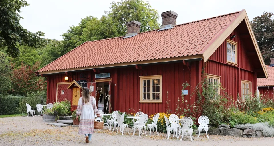 Kvinna går på en grusväg utanför en röd stuga.