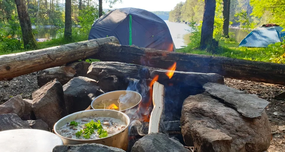 En lägereld med ett blått tält i bakgrunden.