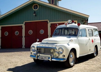 En vit ambulans parkerad framför en grön byggnad.