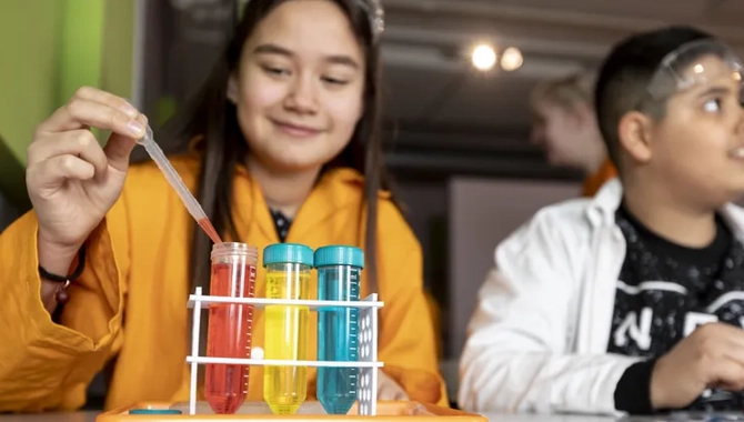 Två barn som sitter vid ett bord och gör ett experiment med provrör med olika färger.