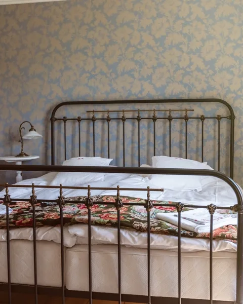 Dubbelsäng med järnram, blommiga taper i bakgrunden.