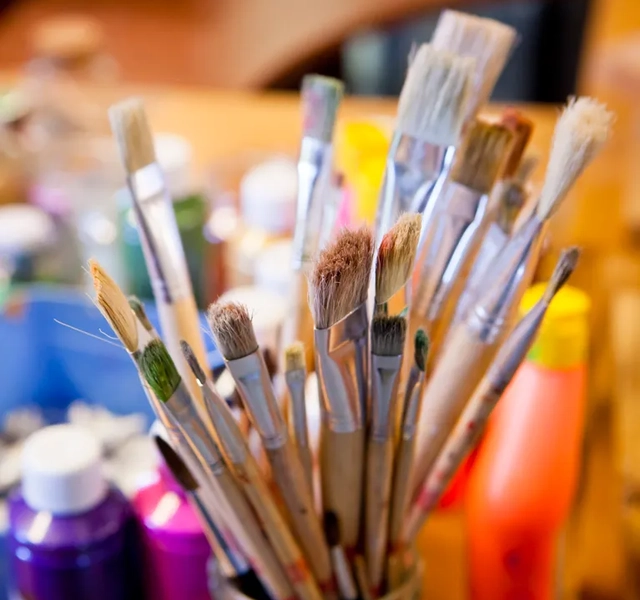 En kopp fylld med massor av färg och penslar.