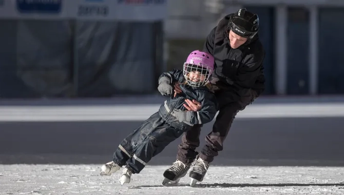 En man åker skridskor och håller ett barn som åker framför honom.