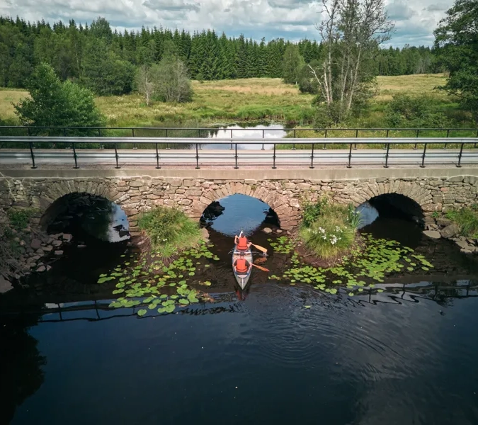 En person i en kanot på en flod under en bro.