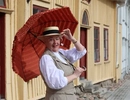 En kvinna i klänning och hatt som håller ett rött paraply.