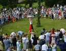 Människor som står i ring runt midsommarstång