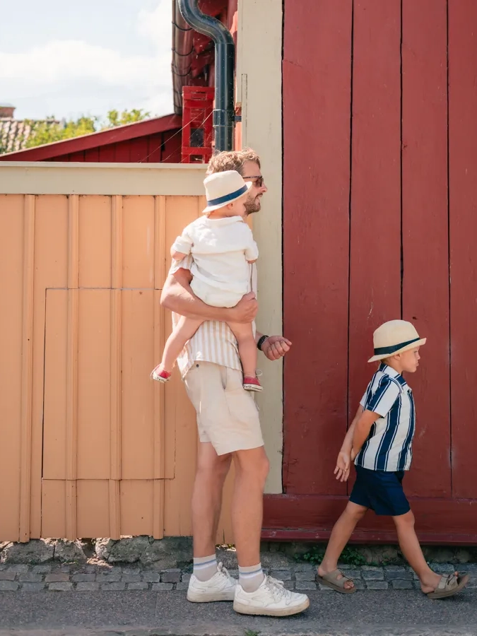 En man håller ett barn medan han står bredvid en röd byggnad.