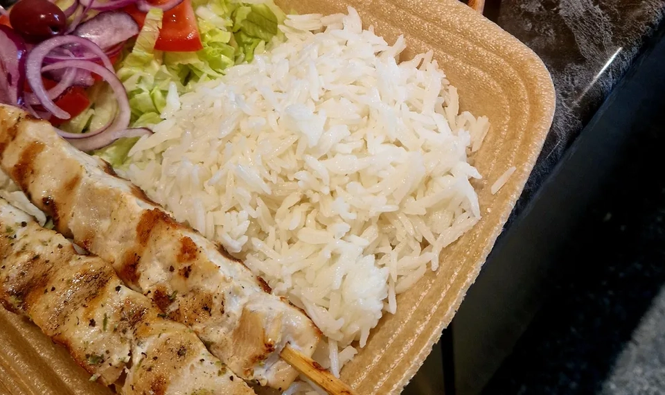 Några brickor fyllda med ris, sallad och grillspett på en disk.