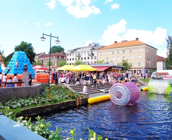 En flod med massor av människor bredvid höga byggnader.