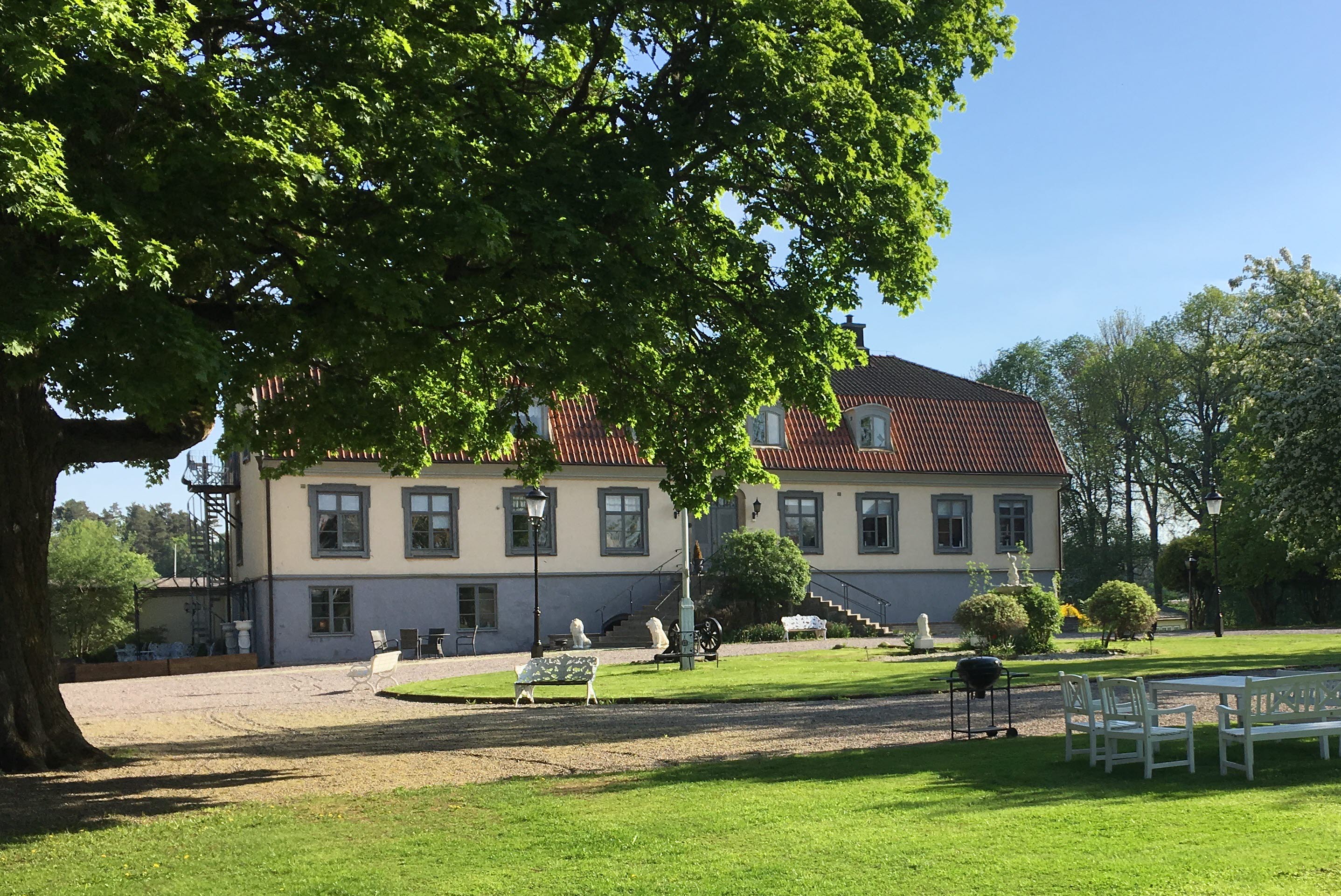 Herrgårdsbyggnad omgiven av gröna träd.