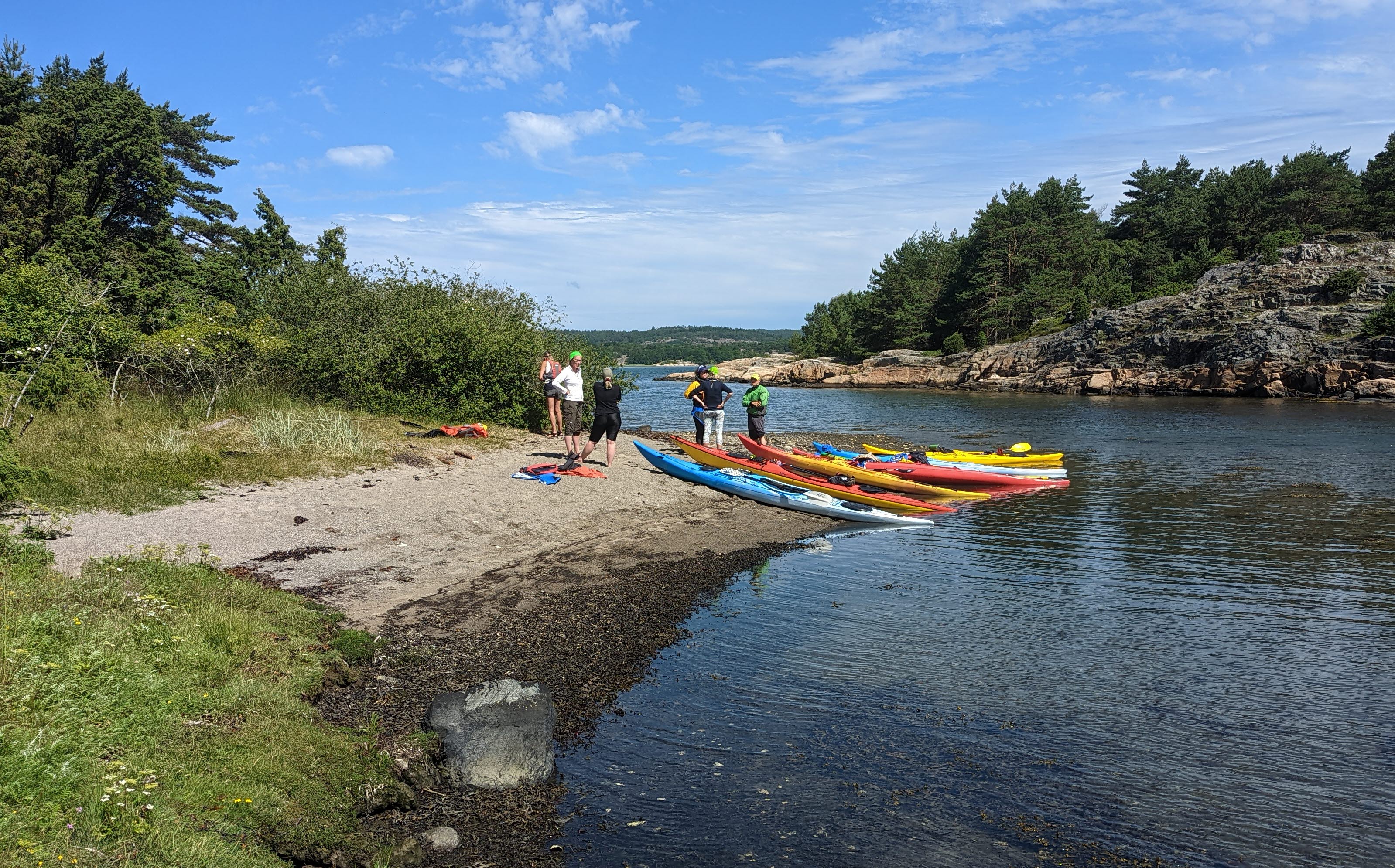 En grupp kajakpaddlare från Balanspunkten – Kajak i Grundsund landstiger på en naturskön och lummig strand i Bohusläns skärgård