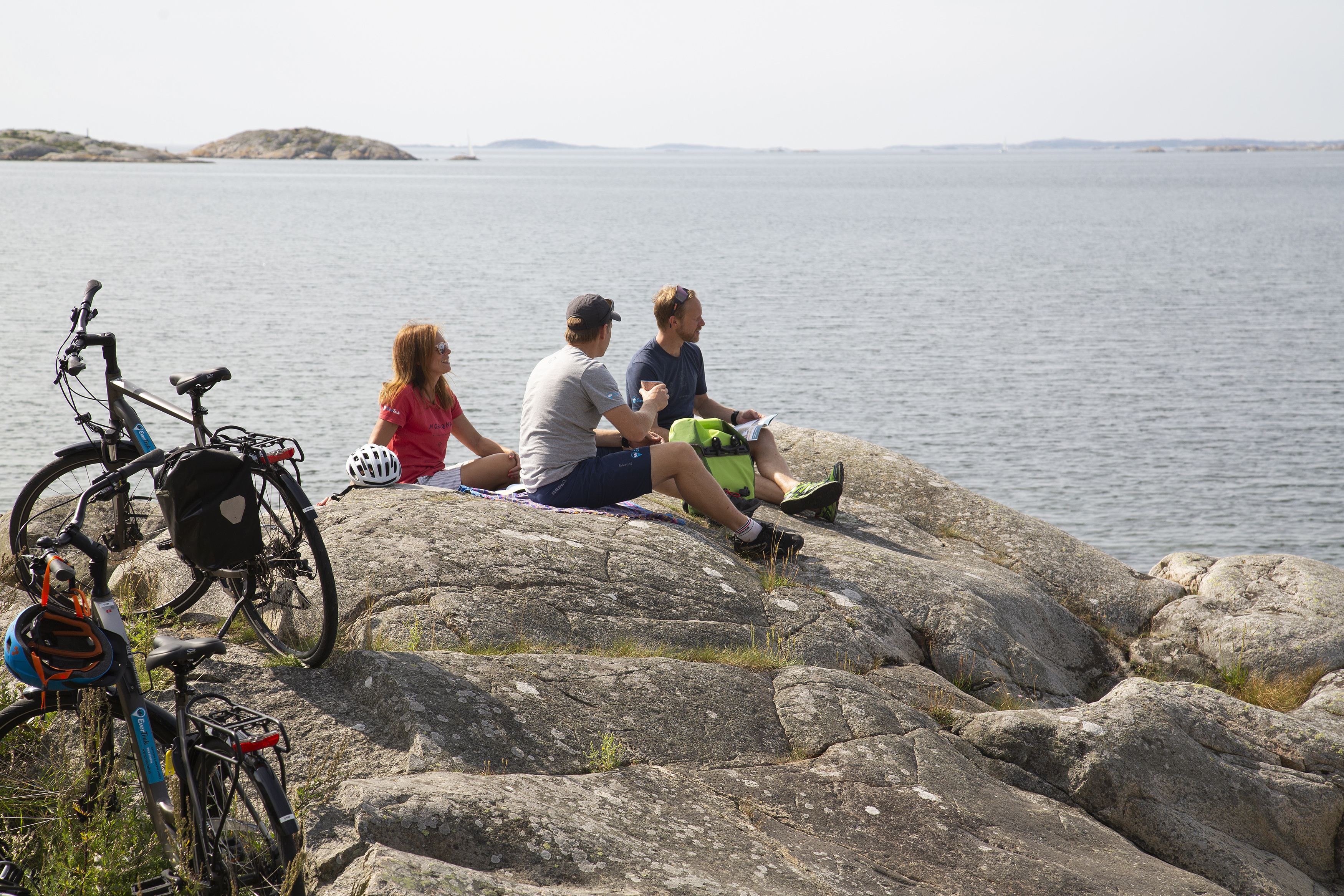 Tre cyklister som har fikapaus på klipporna vid havet.