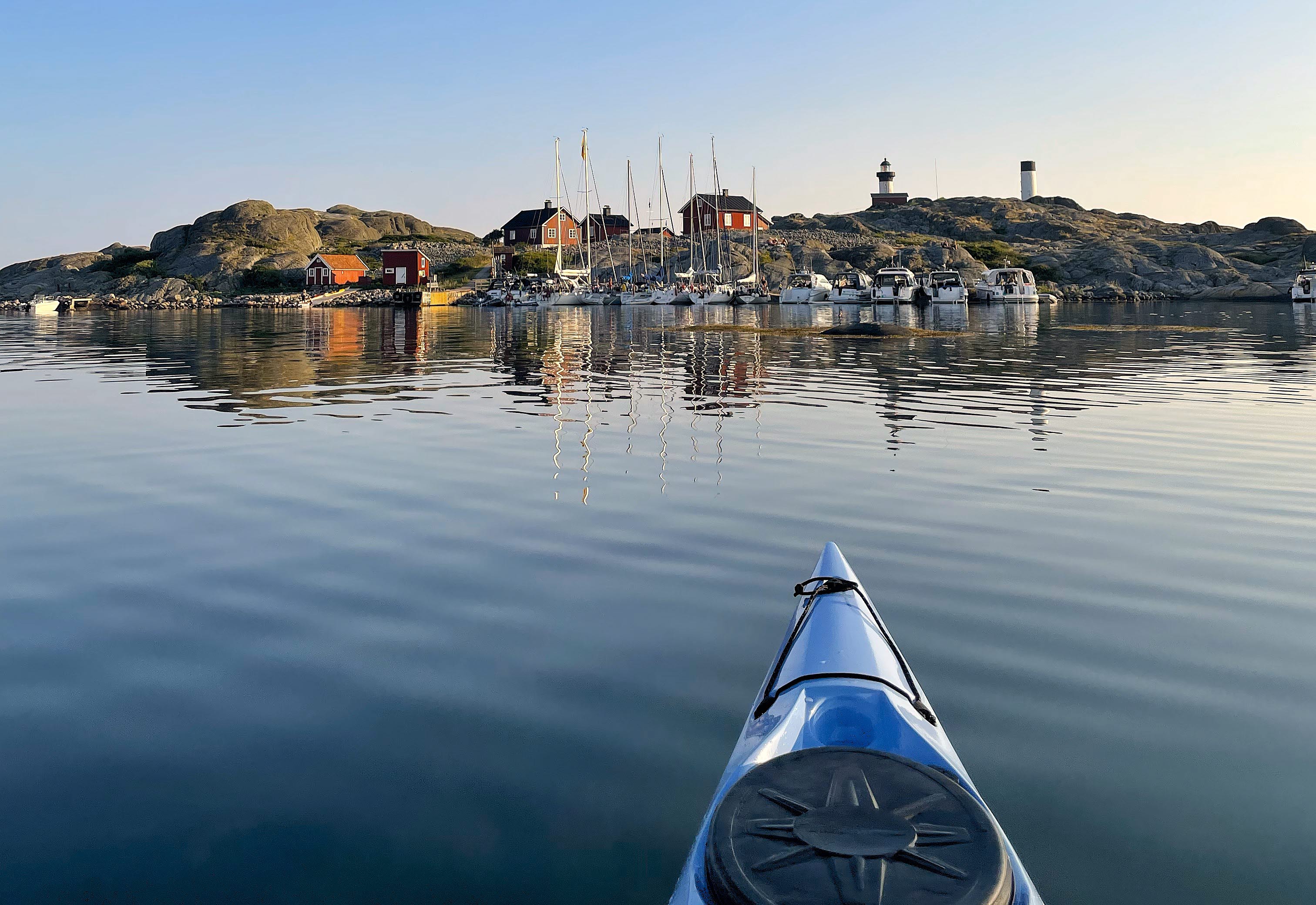 Fören på en kajak i vackert kvällsljus framför en bebodd ö