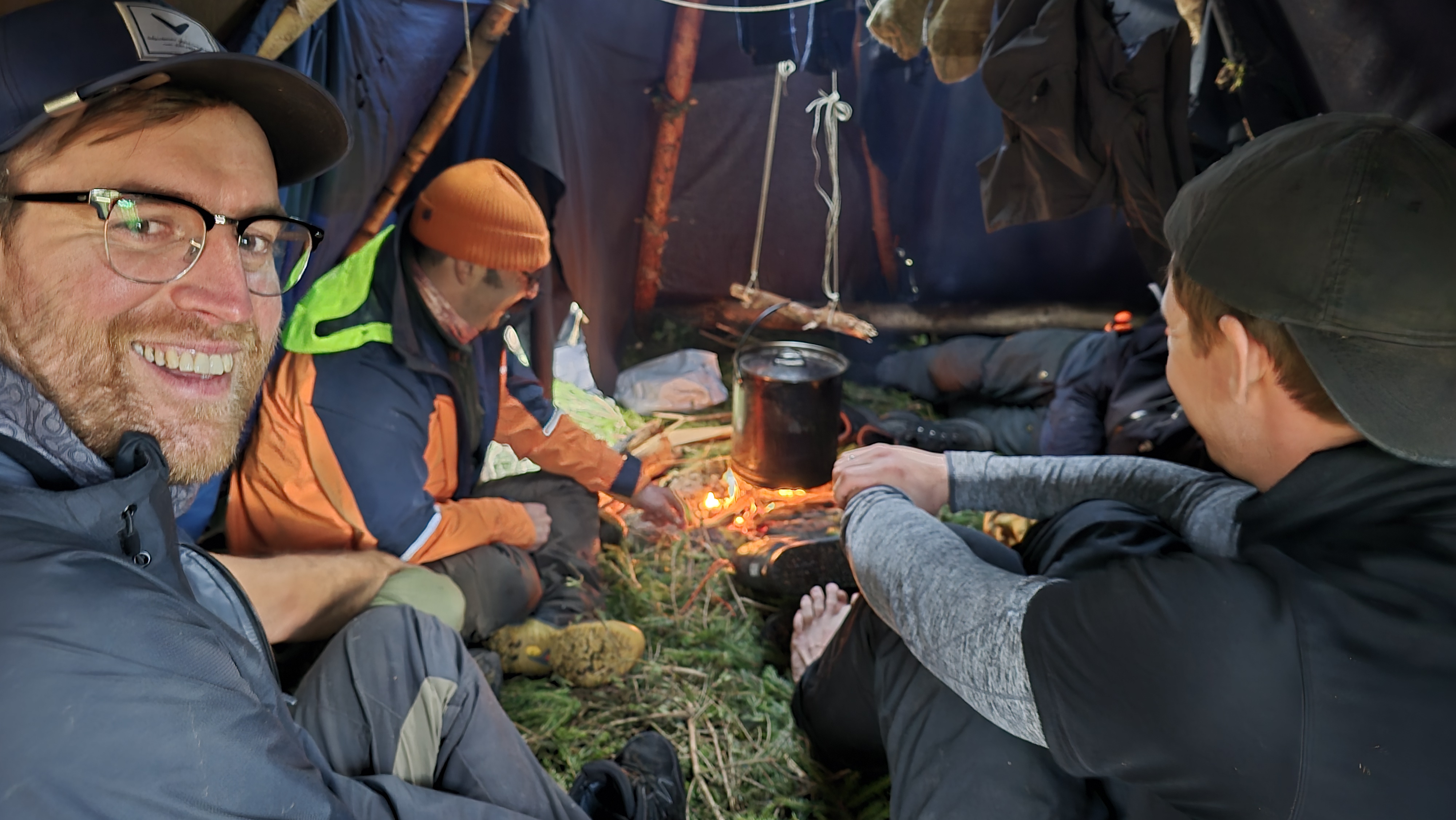 Glada människor i ett tält runt lägerelden - överlevnadskurs med All in Nature Sweden