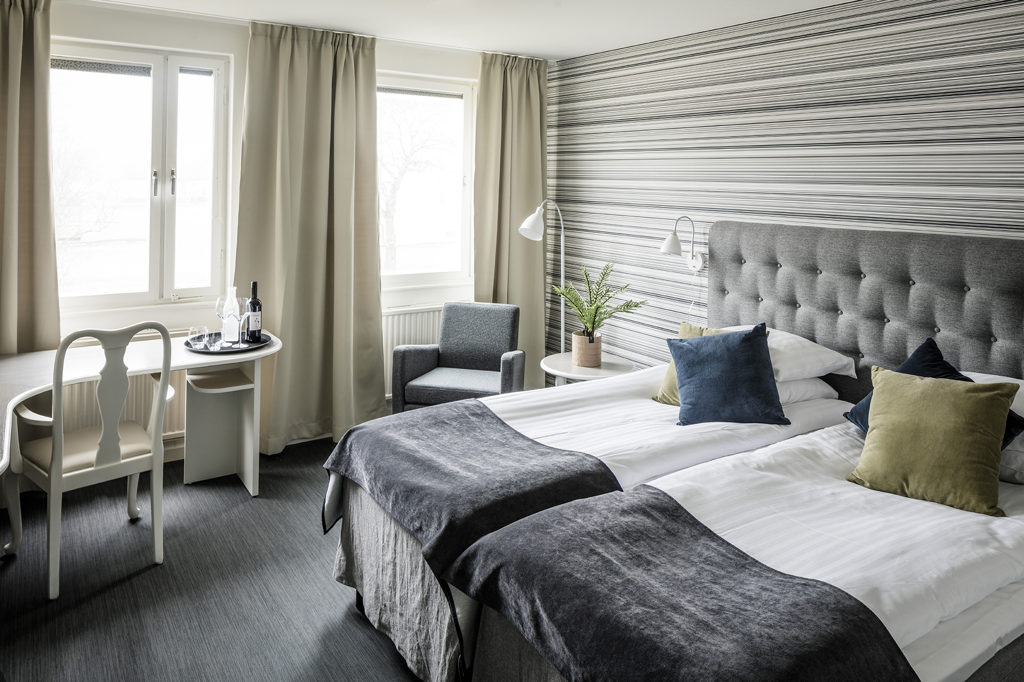 Dubble sized bed, a table and chairs in a bright room with soft colours at Hotel Falköping.