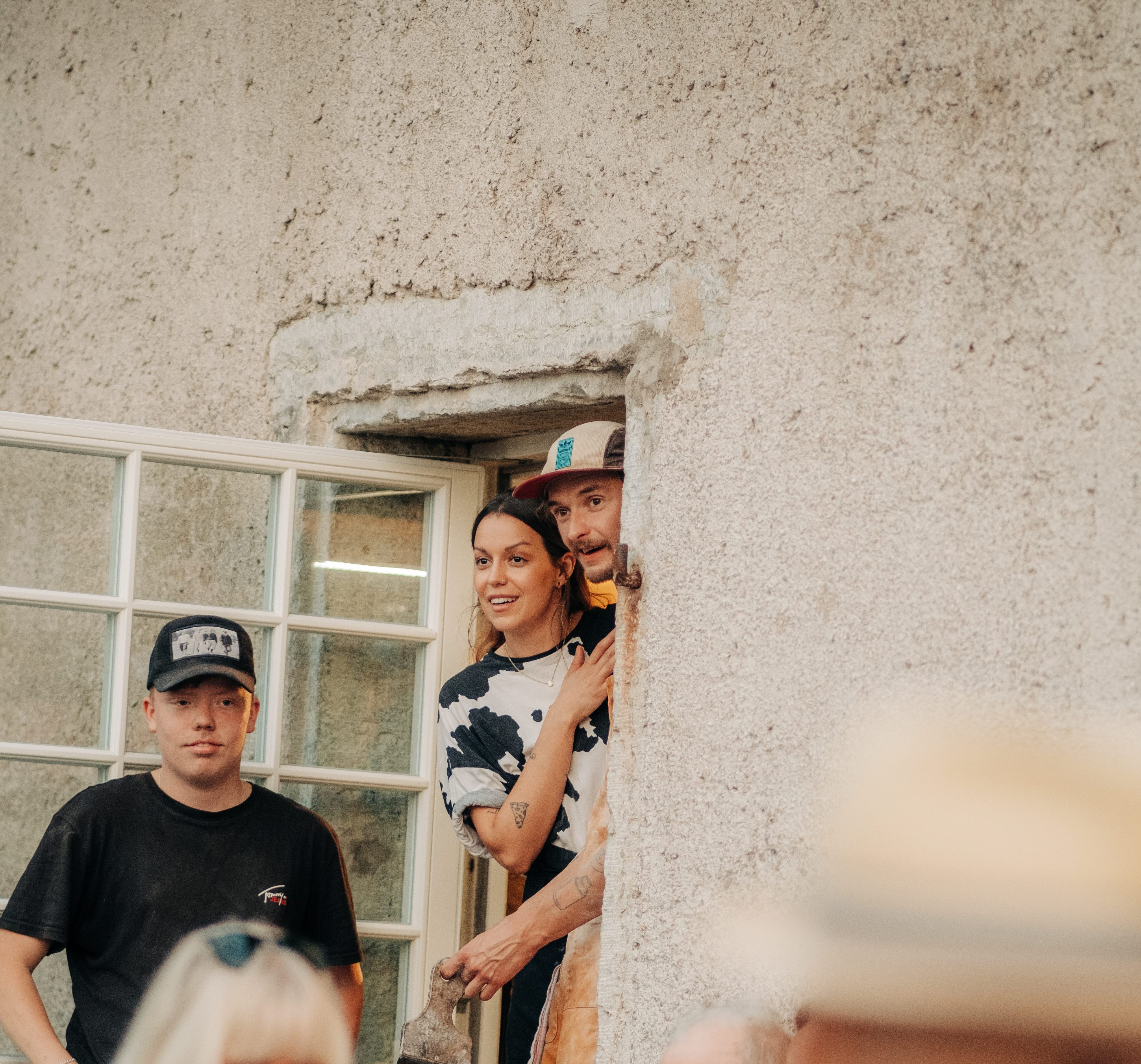 Krögarparet Sara och Filip tittar ut genom ett spröjsat fönster över gästerna på utomhusserveringen på Vedens Lustgård