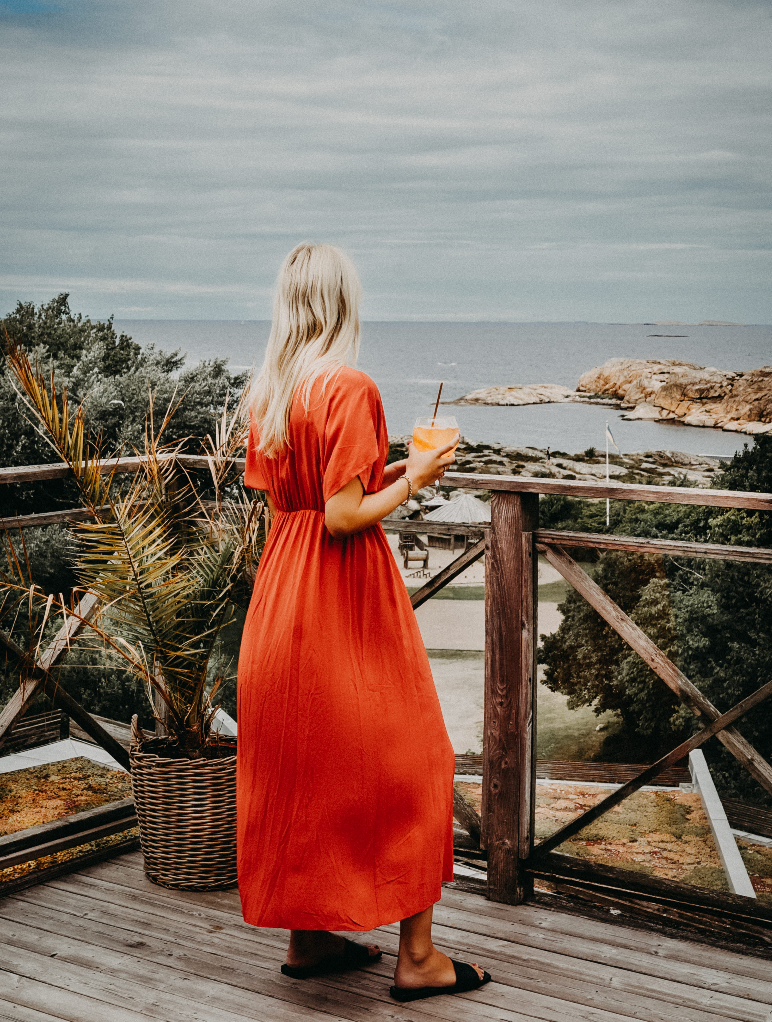 Woman with a drinking glass and tomato red summer dress admires the beautiful sea view from the spa terrace at Hotell Smögens Hafvsbad