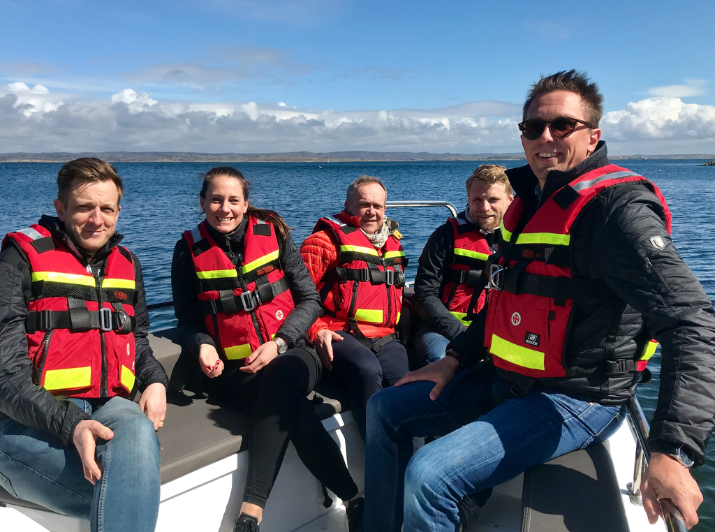 Fem personer med flytvästar sitter i en båt.