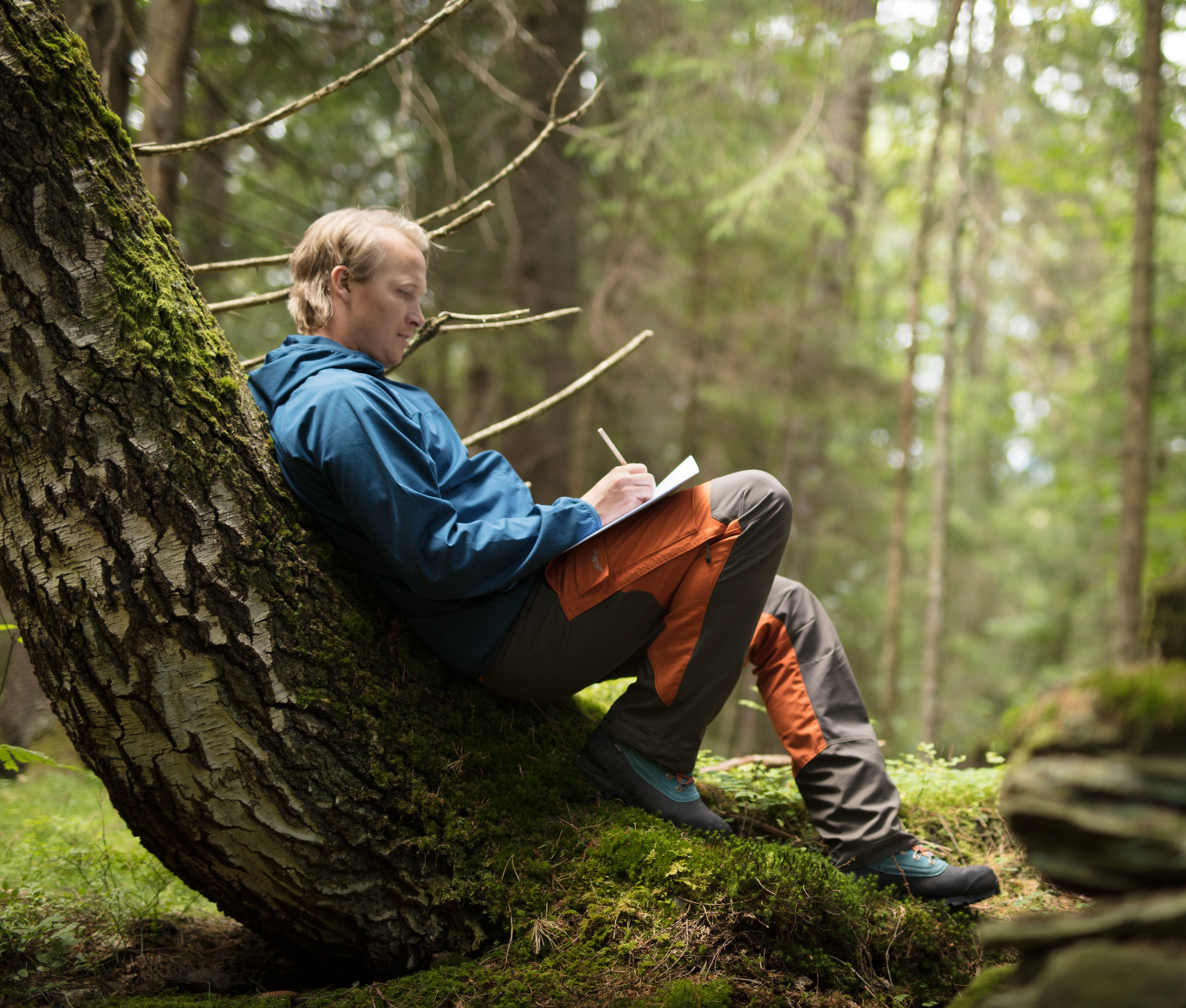 En man lutar sig mot ett träd i skogen.