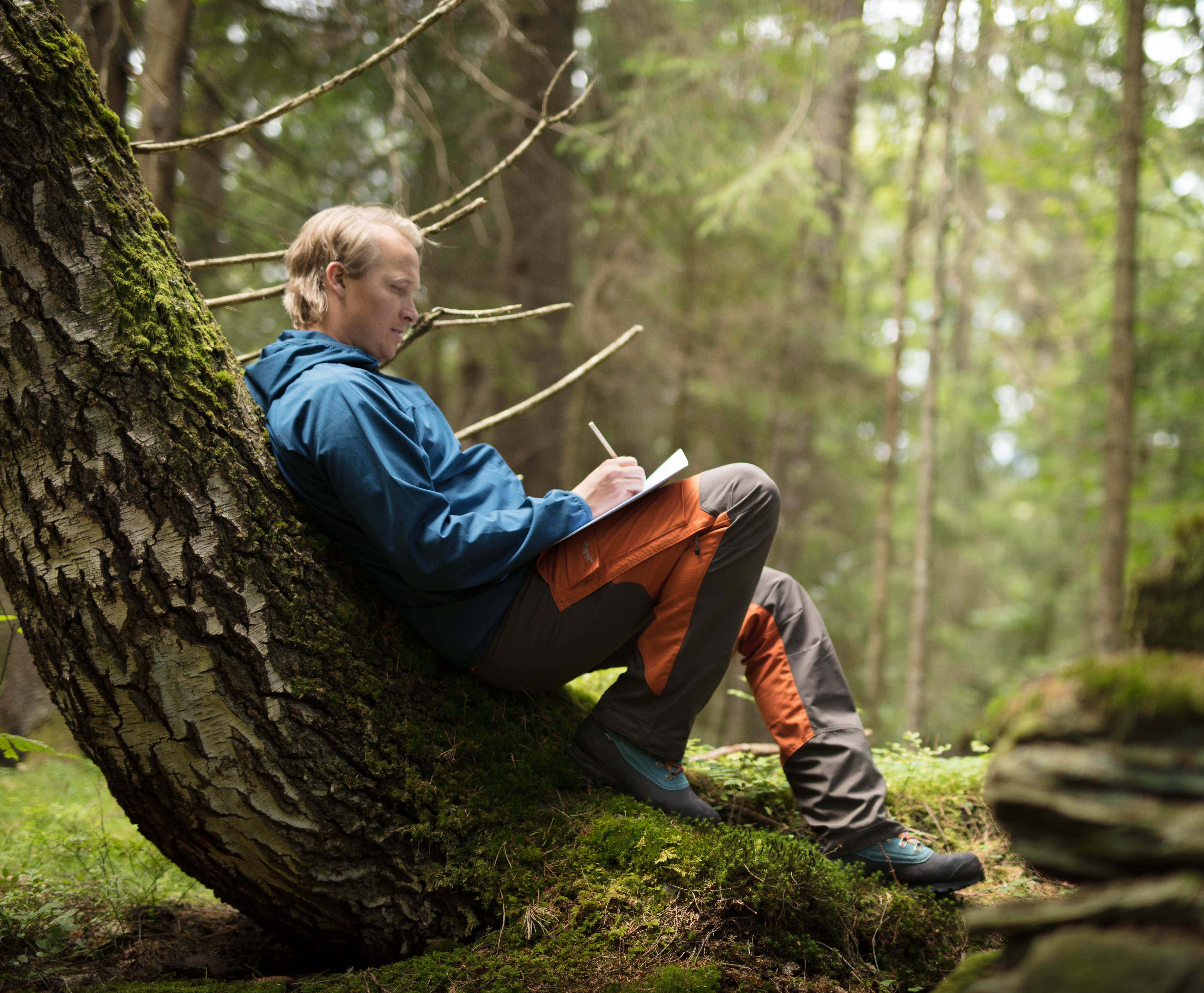 A man leans against a tree in the forest.