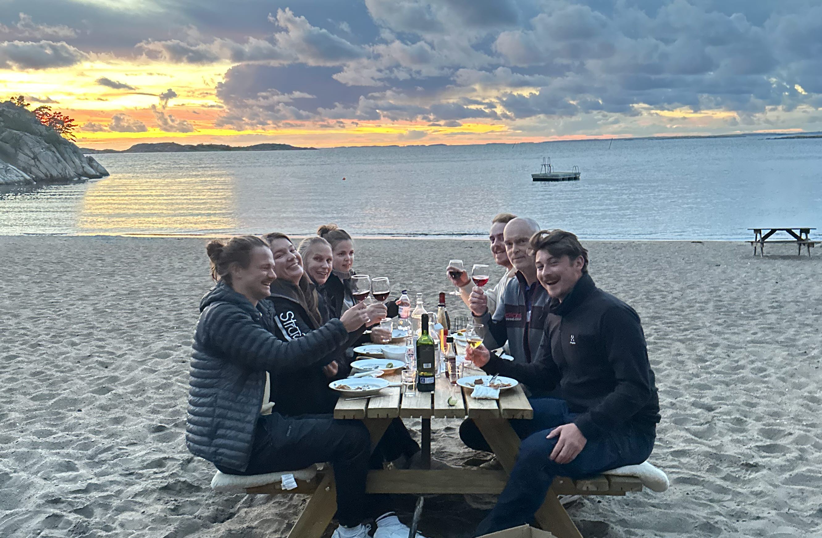Grupp som sitter och äter middag vid ett picknickbord på stranden