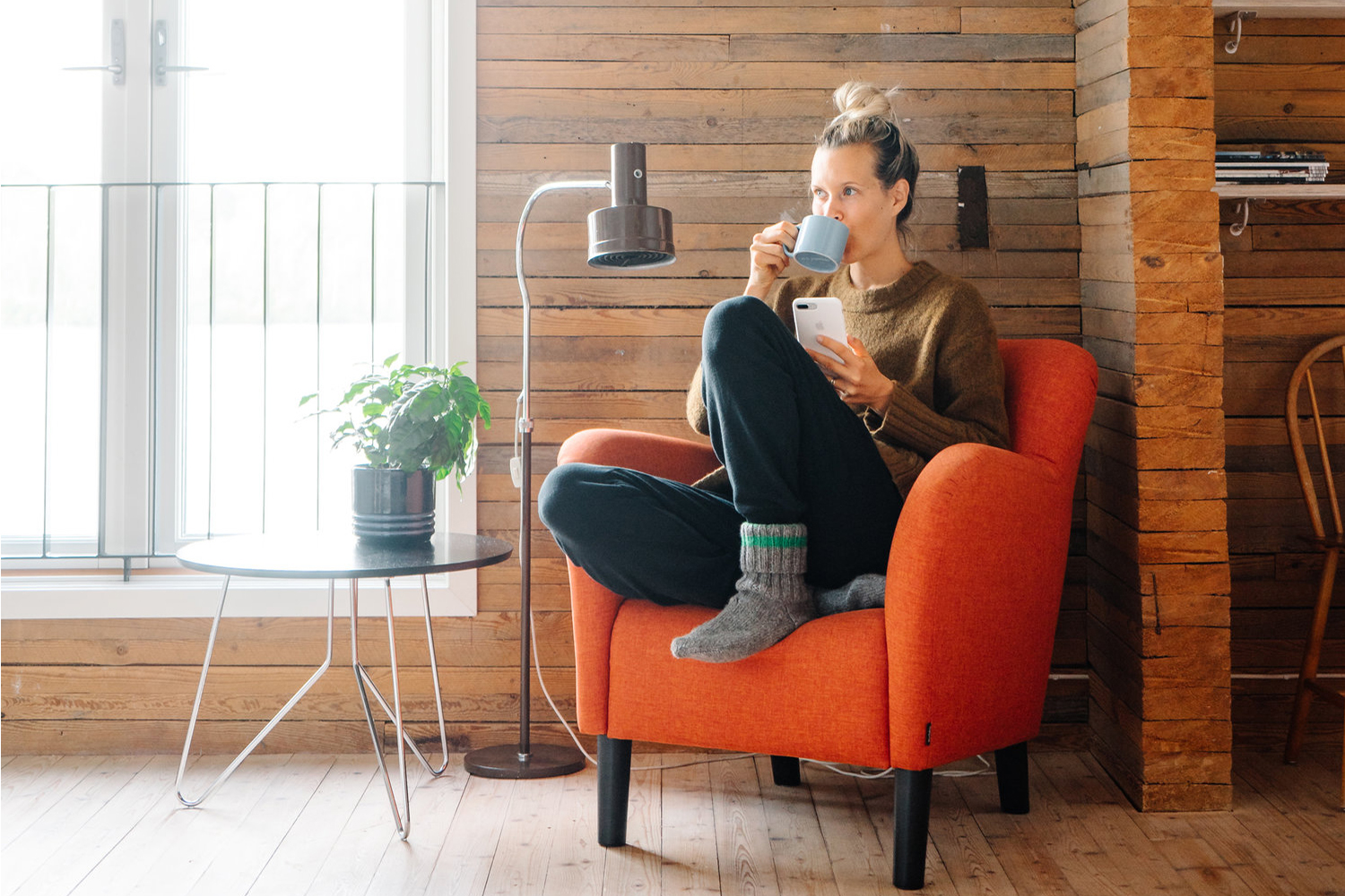 Tjej sitter i en fåtölj och dricker ur en stor kaffemugg.