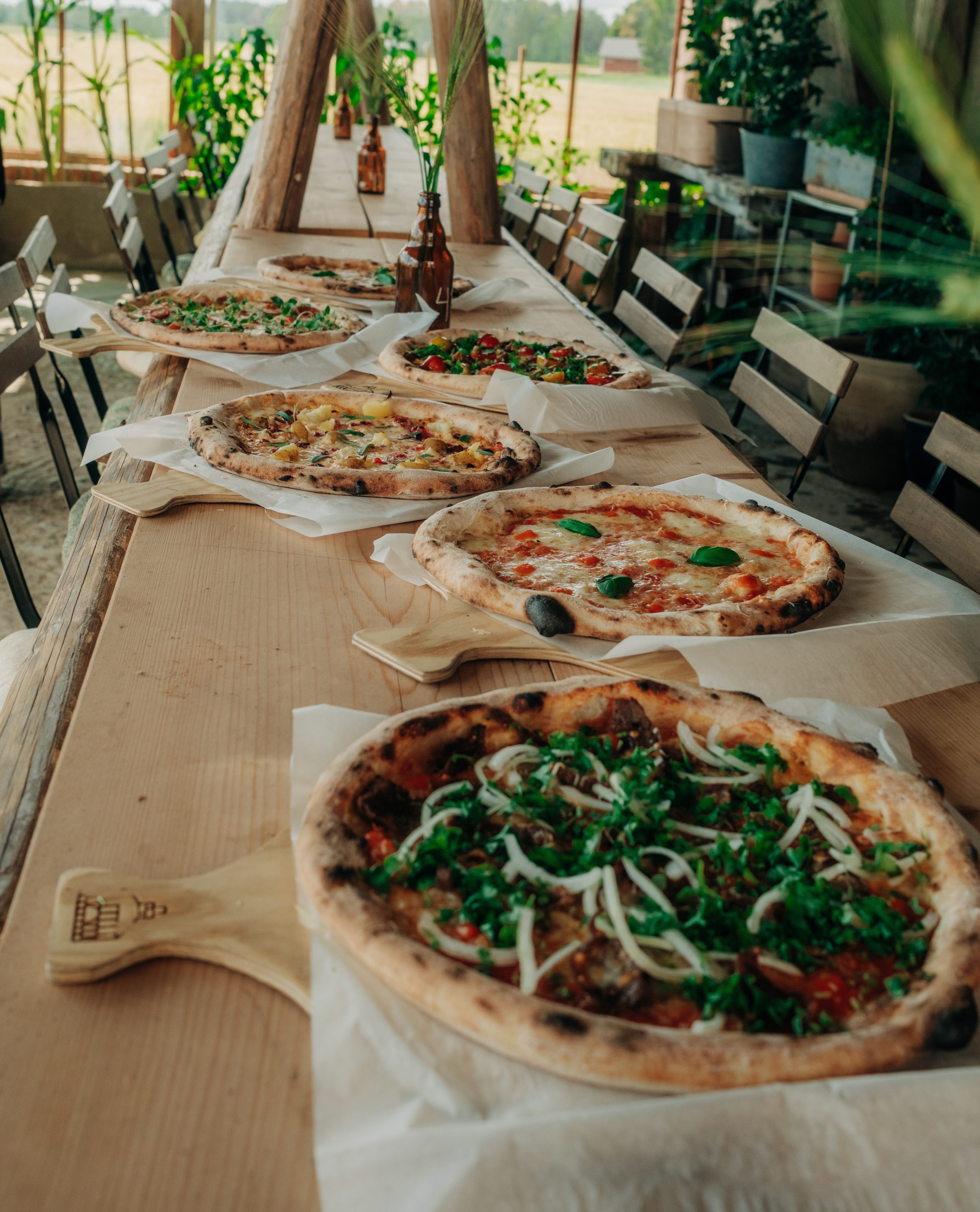 Rustika långbord i trä med uppdukade pizzor i Vedens Lustgårds restaurang