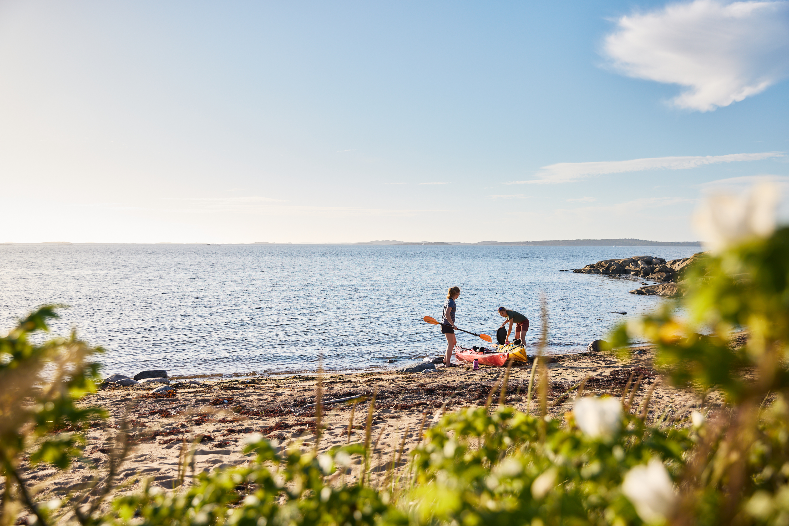 Två kvinnor drar upp sina kajaker på en strand.