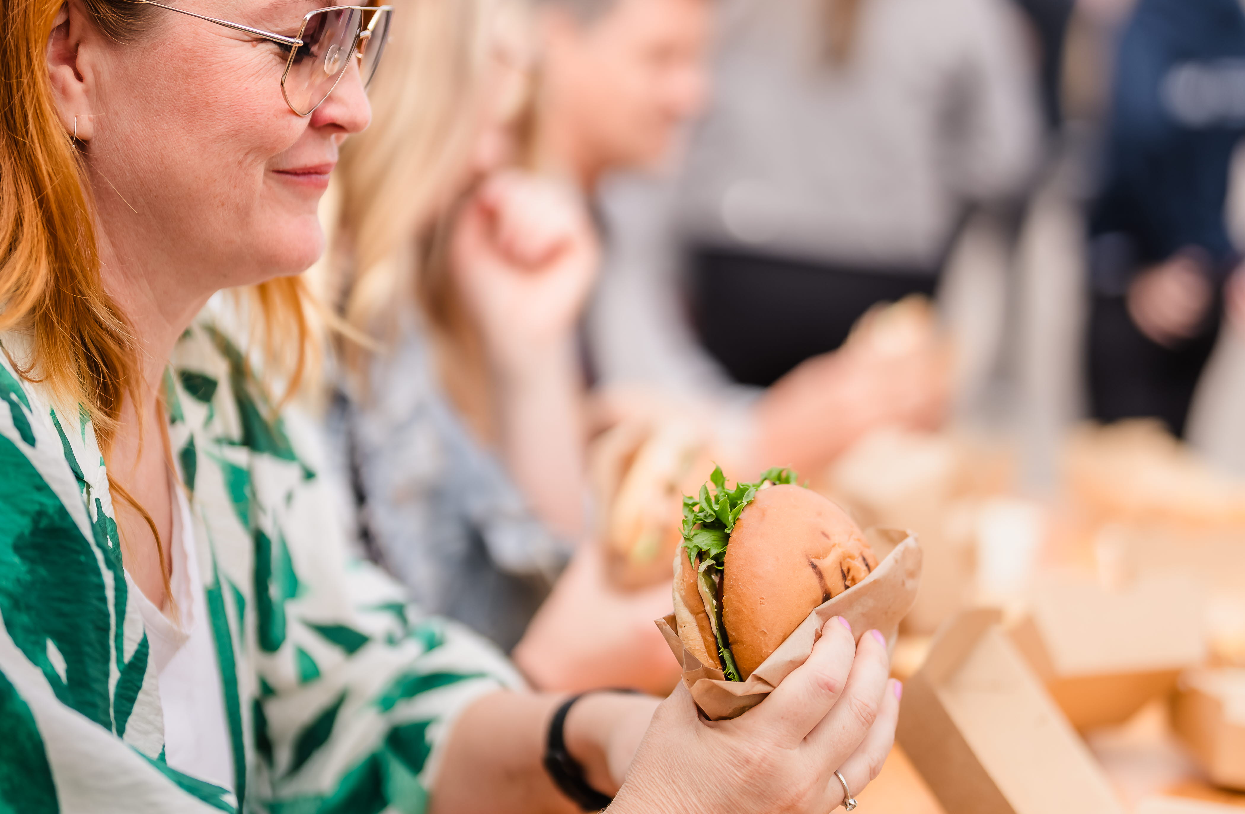 Kvinna sitter vid ett träbord och äter en hamburgare.