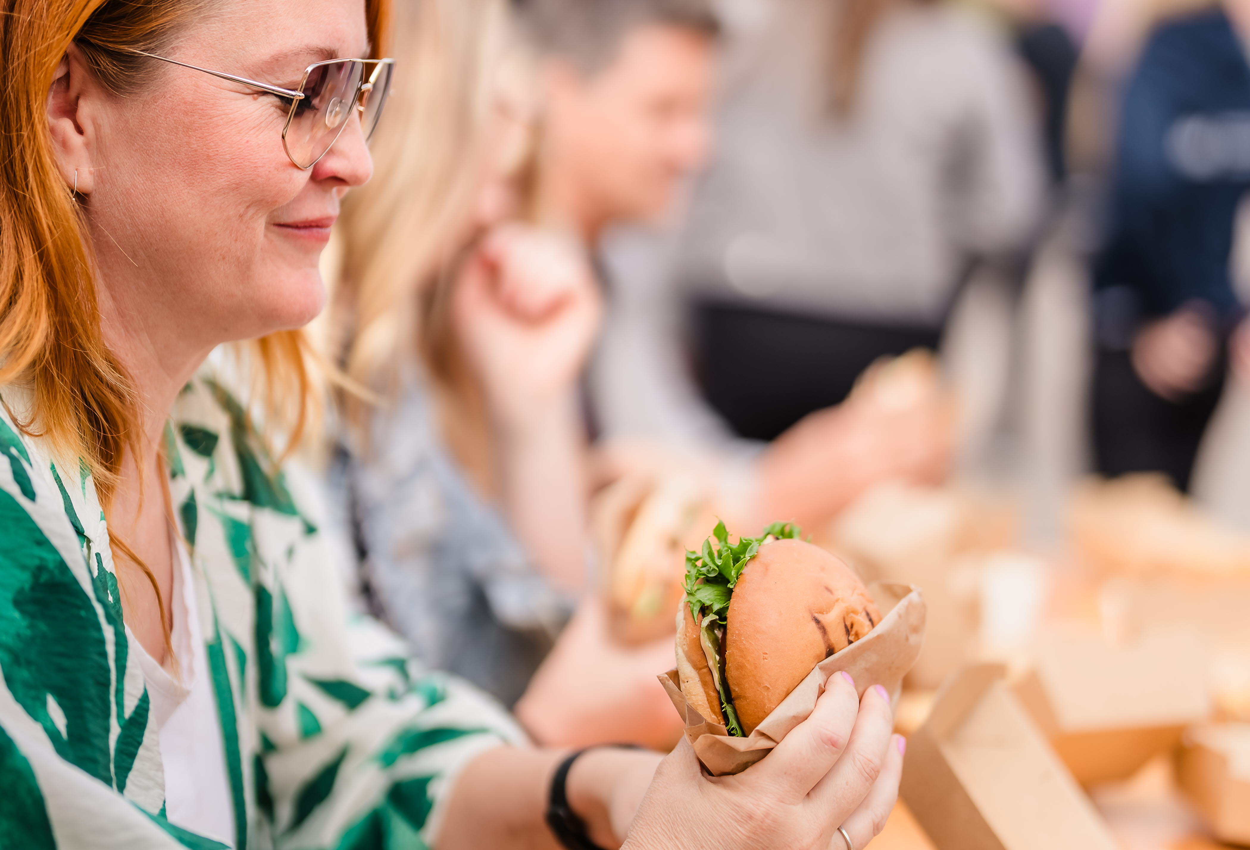 Kvinna sitter vid ett träbord och äter en hamburgare.